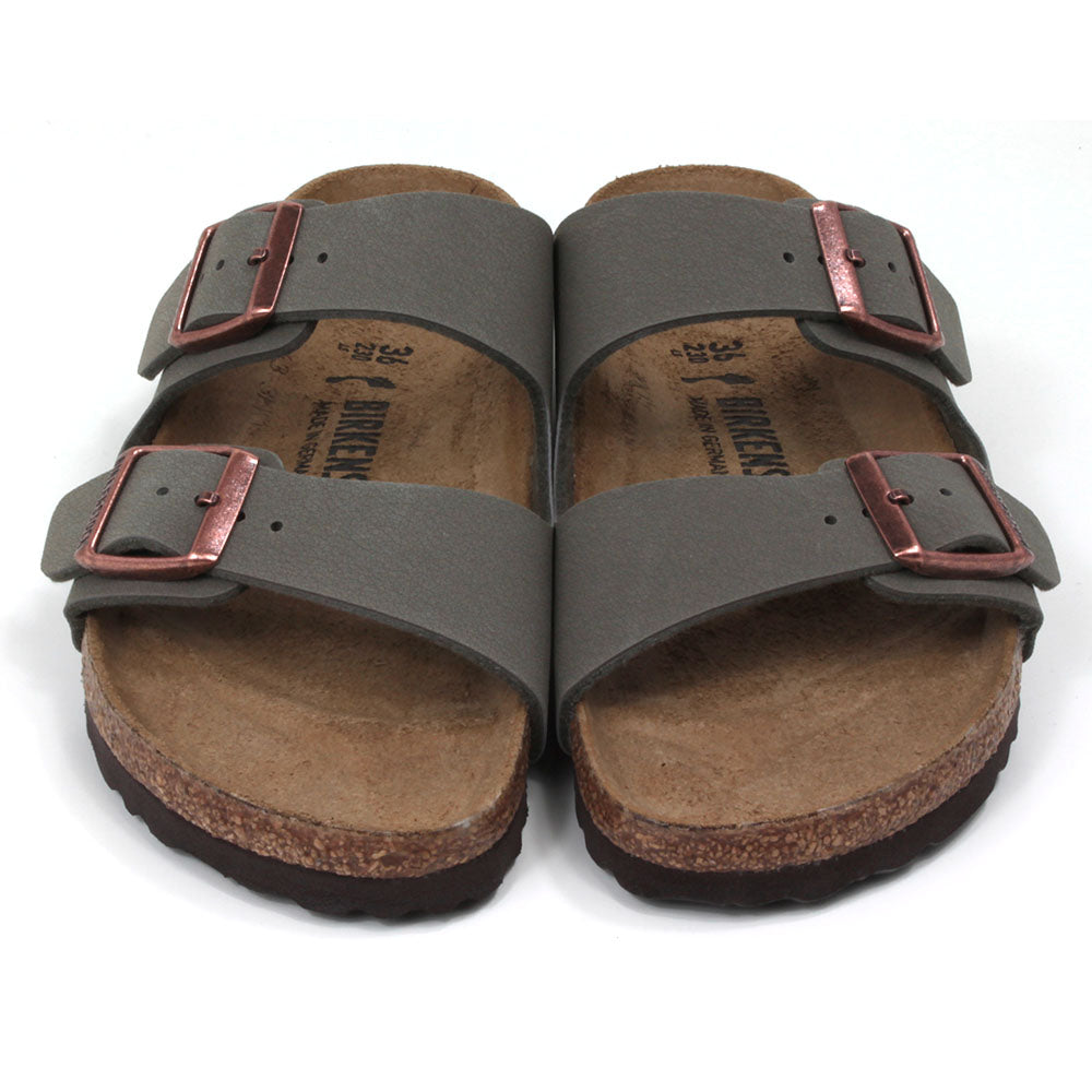 Birkenstock stone coloured Arizona sandals. Two straps over foot adjusted by copper coloured buckles. Open back. Sculpted cork  soles and footbed. Front view.