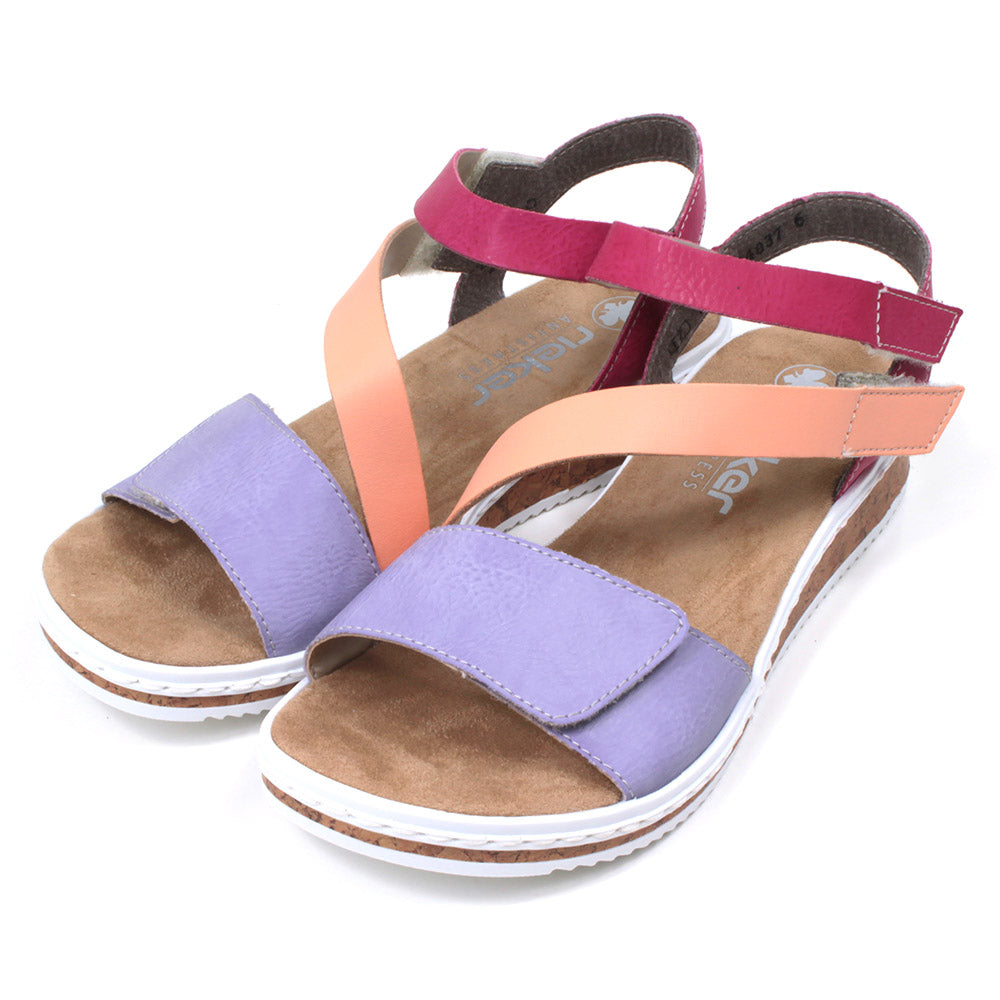 Rieker sandals with sand coloured footbed. Violet, orange and rose pink straps which adjust and fit with Velcro. Soles have white edging. Angled view.