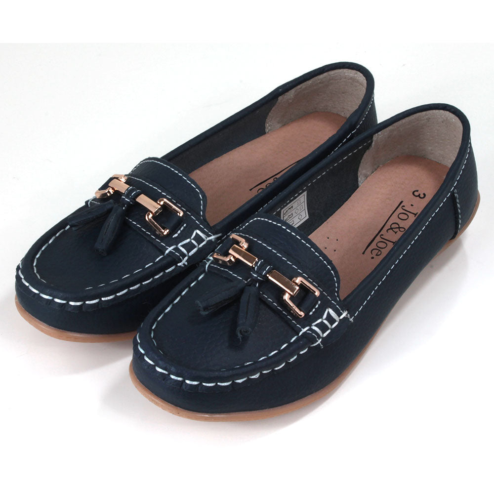 Joe and Jo Nautical moccasin slip on style shoes in dark blue. Gold decorative buckle with double tassels. White stitching. Rubber soles. Angled view.