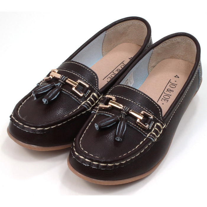 Joe and Jo moccasin style slip on, leather shoes in chocolate colour. Over the foot metallic gold coloured  detail and two matching tassels. Beige rubber soles. Angled view.