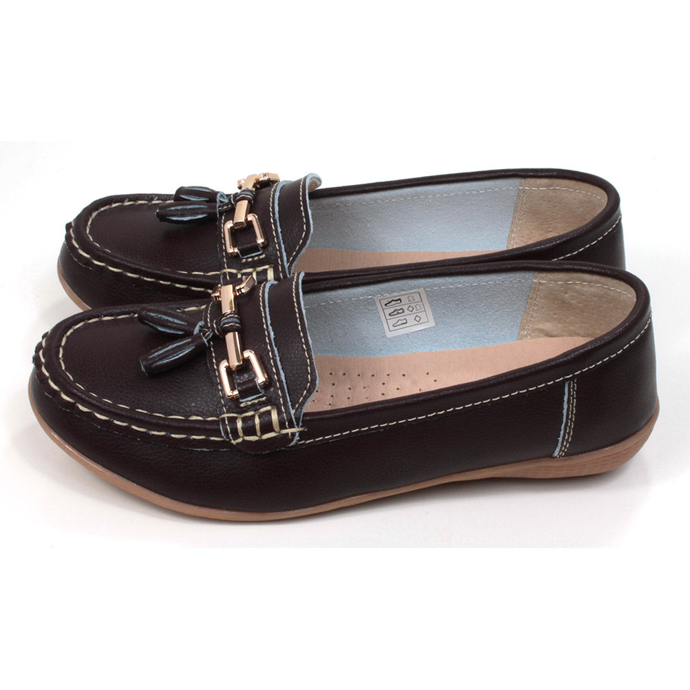 Joe and Jo moccasin style slip on, leather shoes in chocolate colour. Over the foot metallic gold coloured  detail and two matching tassels. Beige rubber soles. Side view.