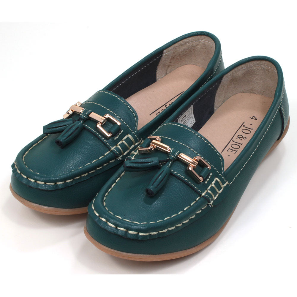 Joe and Jo moccasin style slip on, leather shoes in jasper green colour. Over the foot metallic gold coloured  detail and two matching tassels. Beige rubber soles. Angled view.