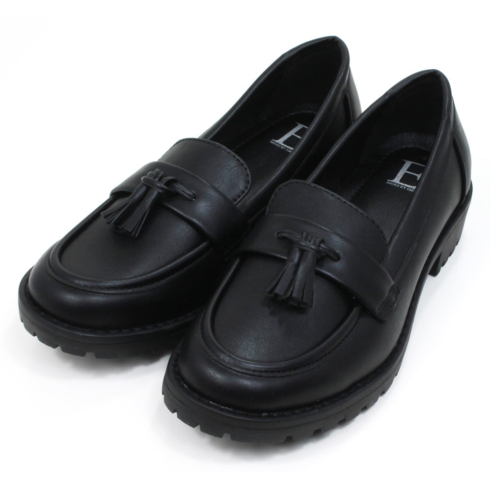 Emma black slip on loafer moccasin style shoes with two tassels on each. Carved, grippy soles. Angled view.