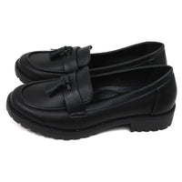 Emma black slip on loafer moccasin style shoes with two tassels on each. Carved, grippy soles. Side view.