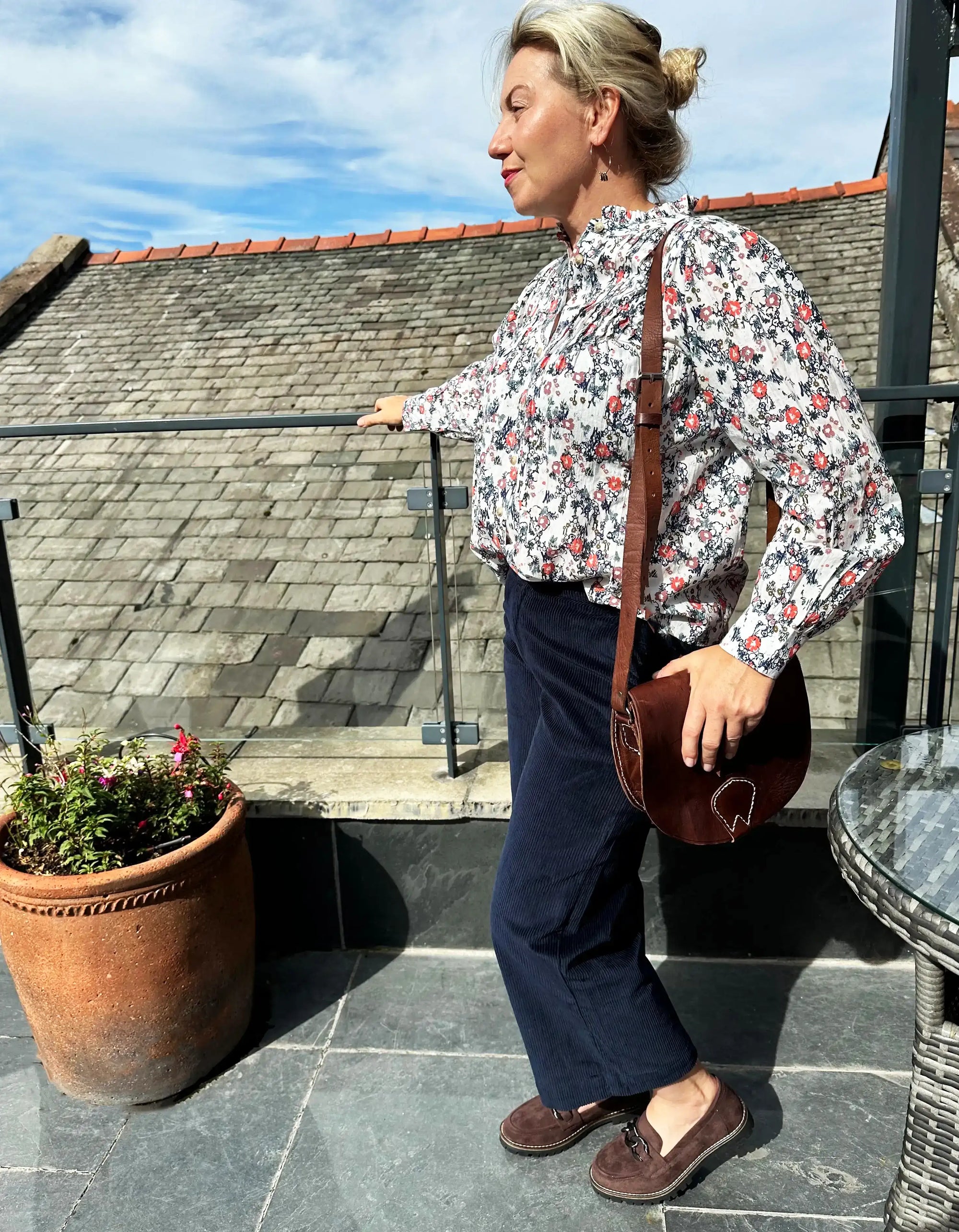 Woman standing on a rooftop with a potted plant and table in the background