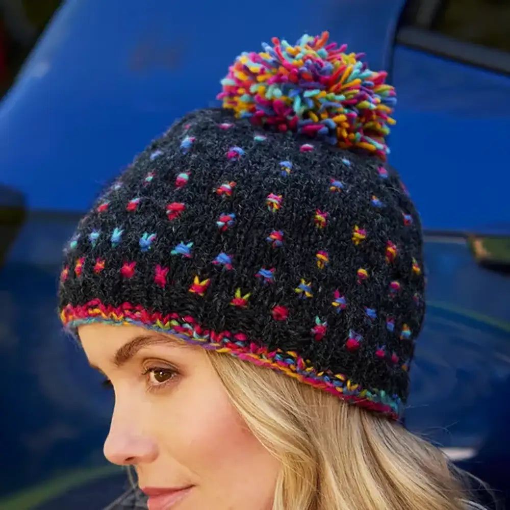 Person wearing a black knit beanie with colorful pom-pom against a blue background