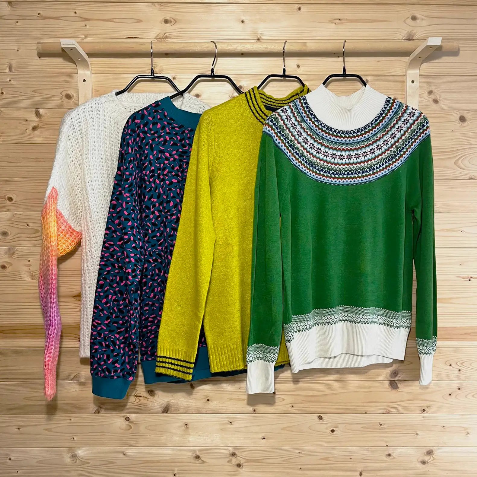 Four sweaters on hangers against a wooden background