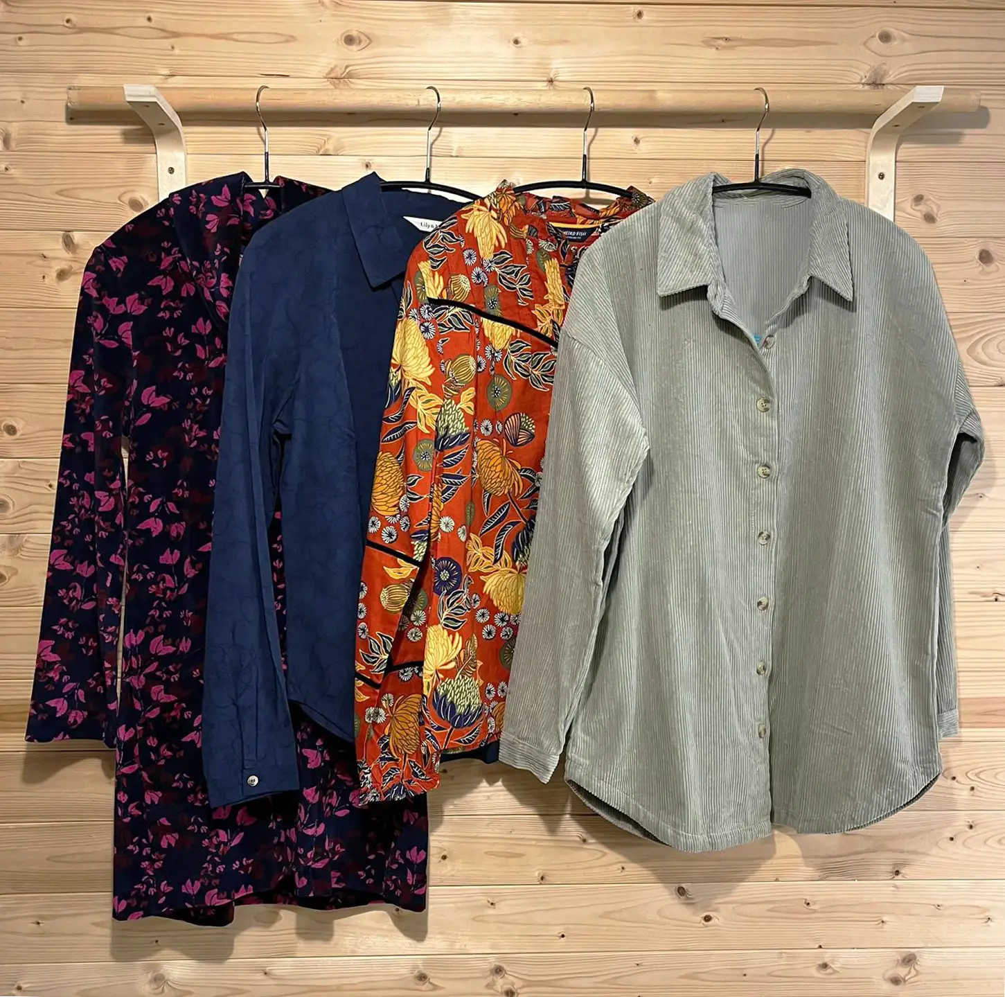 Four shirts on hangers against a wooden wall.