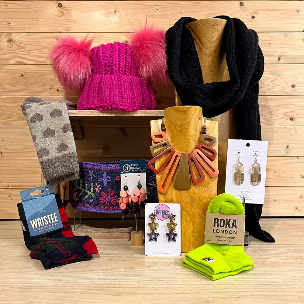 Collection of winter accessories including hats, scarves, socks and earrings on a wooden surface.