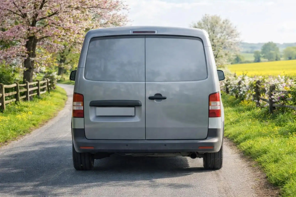 Grey van driving away from the camera down an English sunny lane in spring.