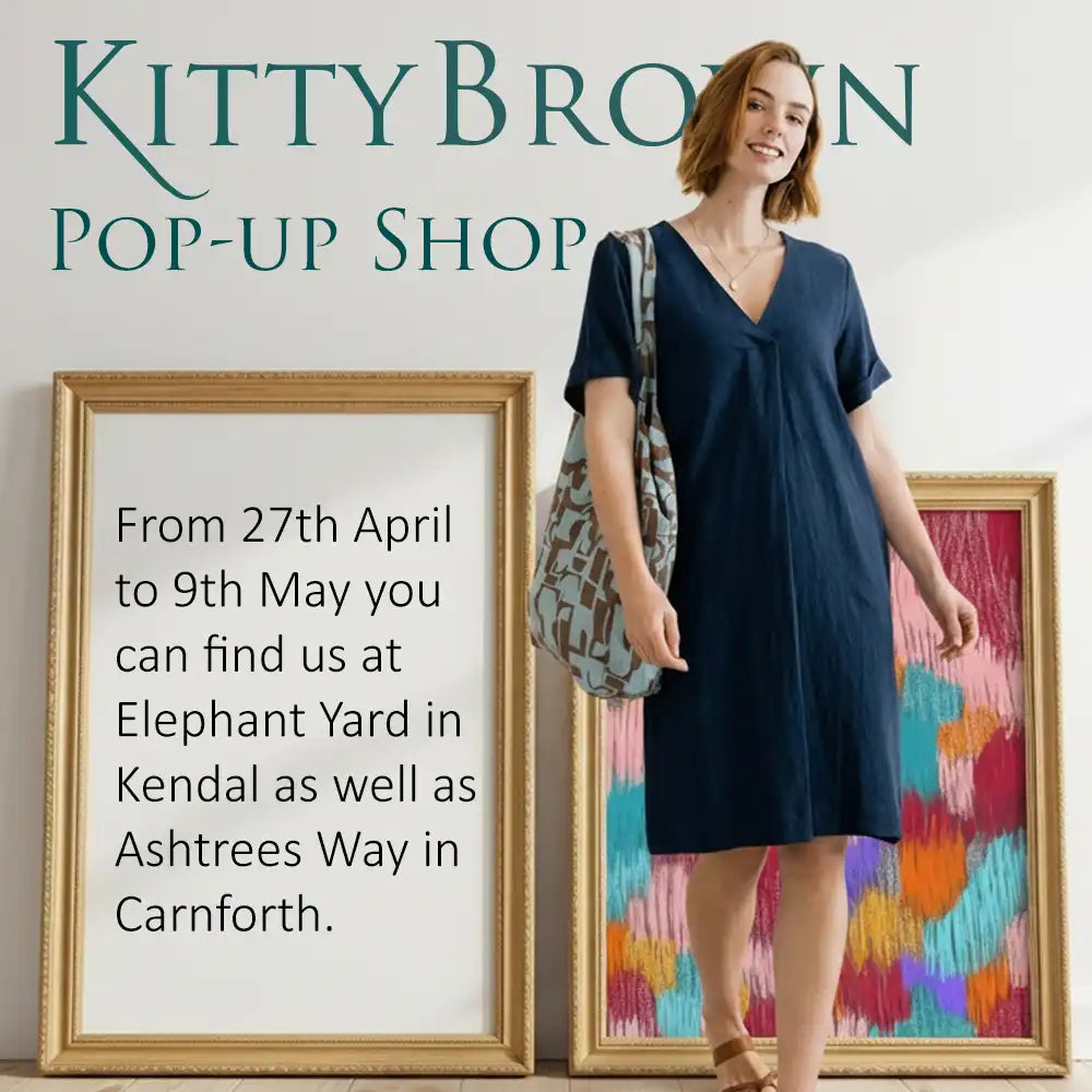 Woman in a blue dress standing next to framed artwork with promotional text for Kitty Brown pop-up shop.