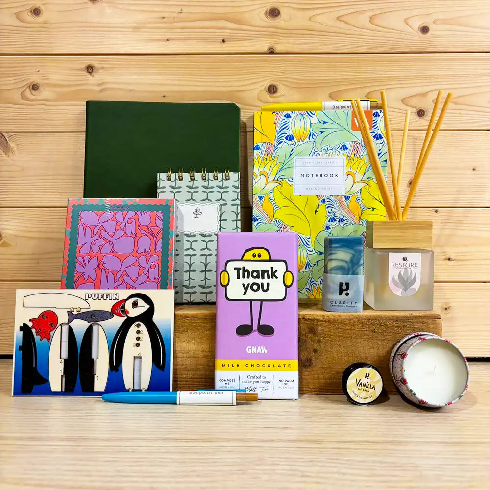 Collection of stationery items including notebooks, a candle, and a small box on a wooden surface.