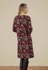 The back of a woman in a floral dress. Dress is a mixture of dark green, purple and beige. 