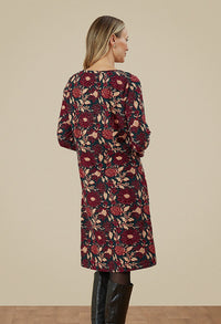 The back of a woman in a floral dress. Dress is a mixture of dark green, purple and beige. 