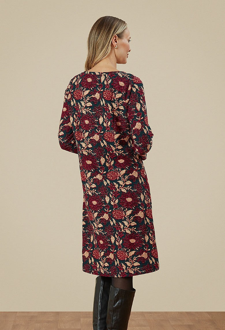 The back of a woman in a floral dress. Dress is a mixture of dark green, purple and beige. 