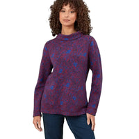 A woman wearing a long-sleeve knit cowl-neck sweater with a red and blue floral pattern, paired with dark blue jeans, set against a solid white studio background.
