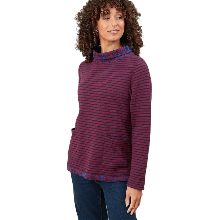 A woman modeling a long-sleeve knit sweater with horizontal burgundy and navy stripes, featuring a patterned mock neck, hem, and pocket trim, paired with dark blue jeans against a solid white background.