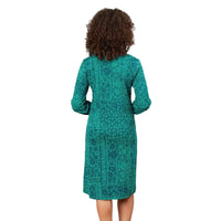 A woman viewed from the back wearing a teal green long-sleeve dress with an intricate dark pattern, set against a solid white background.
