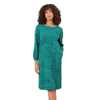 A woman with curly brown hair wearing a teal green long-sleeve midi dress with a tonal abstract pattern and front pockets, standing against a solid white background.