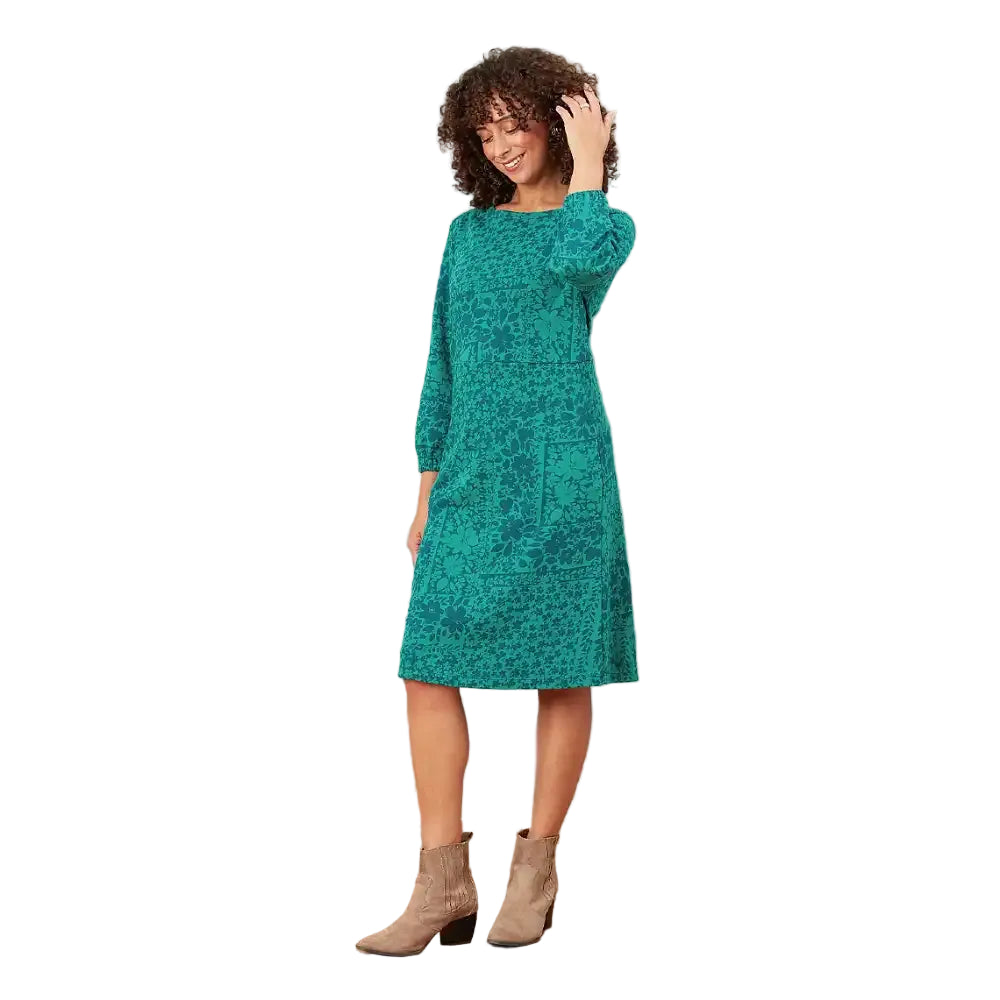A woman modeling a teal green long-sleeve midi dress with a tonal floral pattern, standing against a solid white background.