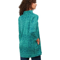 A woman shown from the back wearing a teal patterned long-sleeve tunic top with pockets, set against a plain white background.