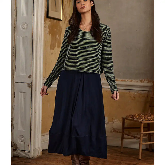 Woman wearing a green and black striped sweater and navy skirt in a room with peeling paint.