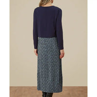 Person wearing a navy long-sleeve top and patterned skirt on a beige background