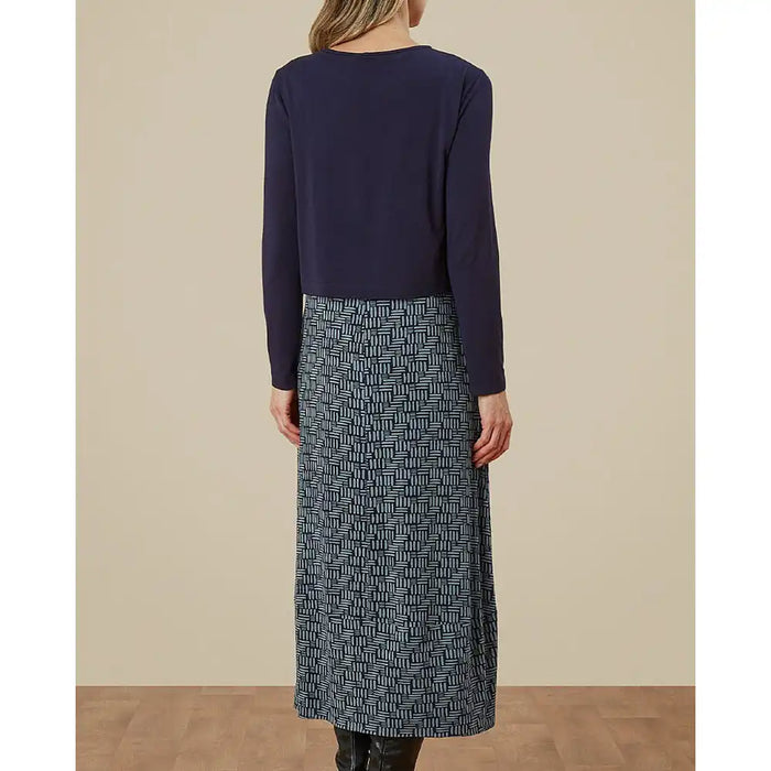 Person wearing a navy long-sleeve top and patterned skirt on a beige background