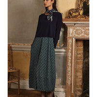 Woman wearing a black top and patterned skirt in an ornate room.