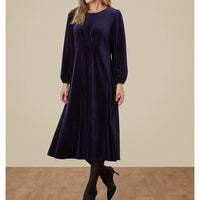 Woman wearing a dark blue dress against a beige wall.