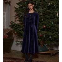 Woman in a dark blue velvet dress standing in front of a decorated Christmas tree.