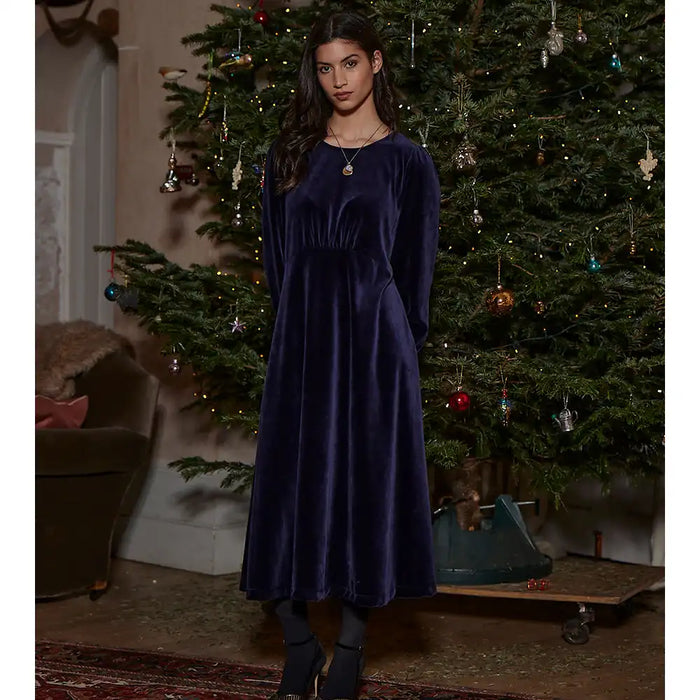 Woman in a dark blue velvet dress standing in front of a decorated Christmas tree.