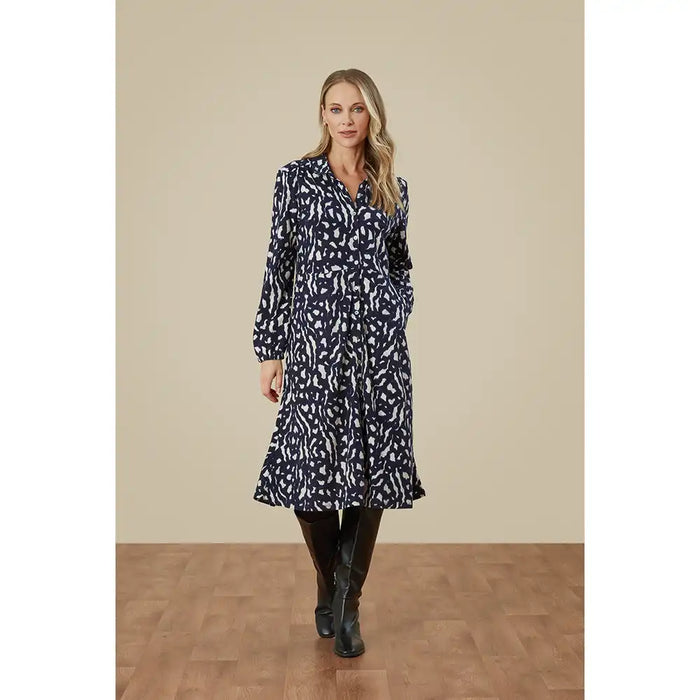 Woman wearing a black and white patterned dress with long sleeves against a beige wall.