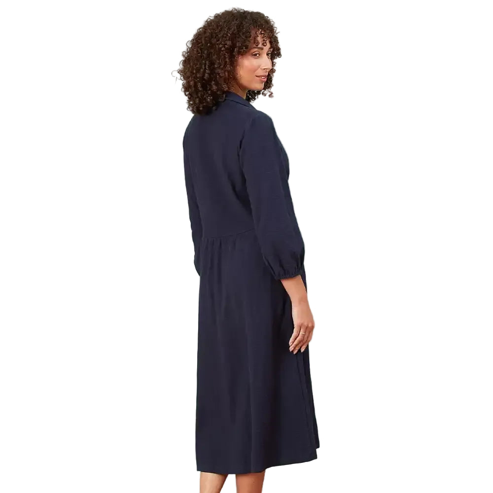 A woman with curly brown hair is shown from the back wearing a dark navy blue midi dress with three-quarter puffed sleeves, set against a solid white background.
