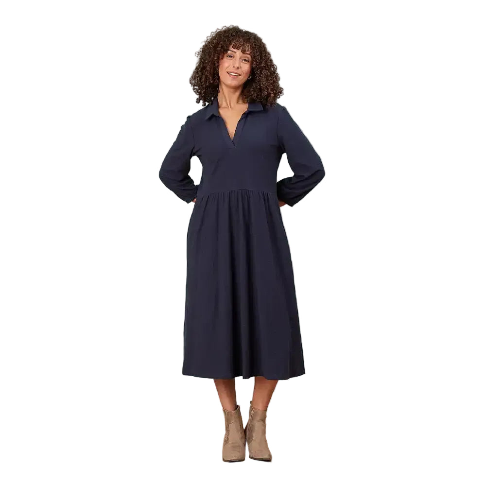 A woman modeling a long-sleeve navy midi dress with a collared neckline and gathered waist, standing in a white environment.