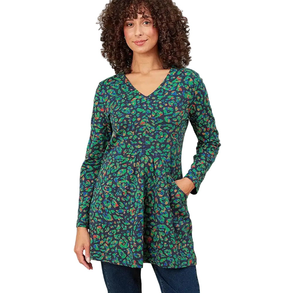 A woman with curly brown hair wearing a long-sleeve V-neck tunic top with a green, blue, and orange paisley pattern, paired with dark blue jeans, against a plain white background.