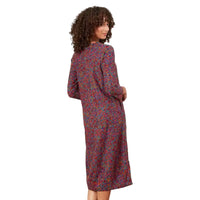 A woman with curly brown hair is shown from the back wearing a long-sleeved midi dress with a dense multicolor abstract print on a muted purple base, set against a white background.