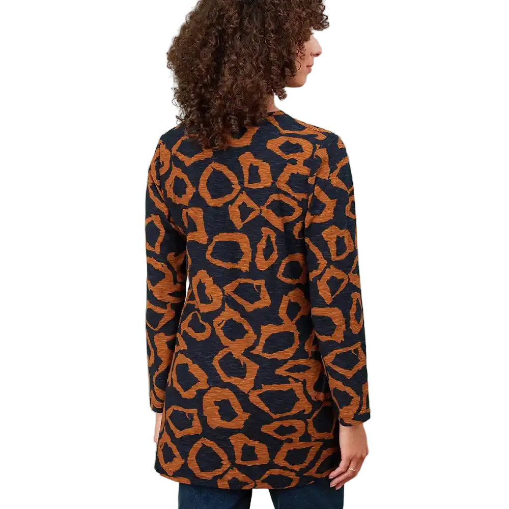A woman shown from the back wearing a long-sleeve tunic top with an abstract organic pattern in orange and black, in a white environment.