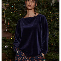 Woman wearing a dark blue velvet top in front of a decorated Christmas tree.