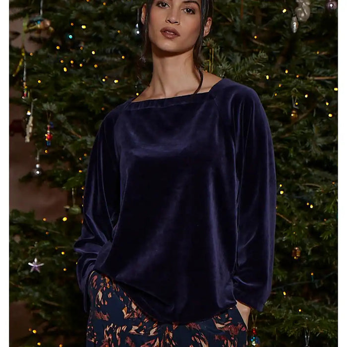 Woman wearing a dark blue velvet top in front of a decorated Christmas tree.