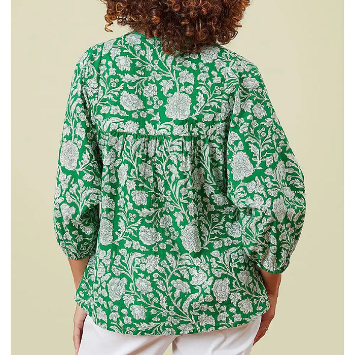 Person wearing a green floral patterned blouse against a beige background