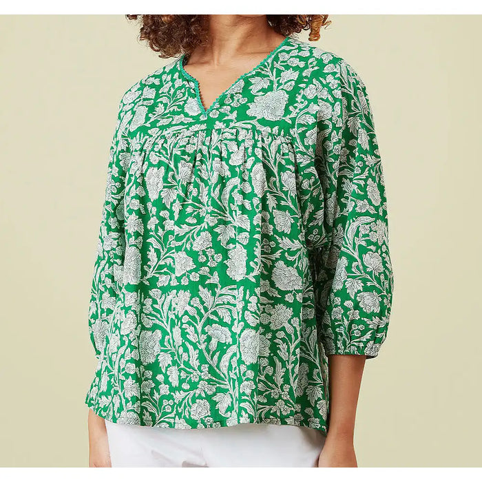 Green floral patterned blouse worn by a person on a beige background