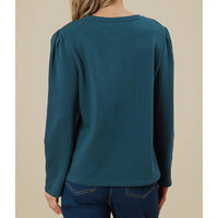 Teal long-sleeve top worn by a person on a beige background
