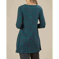 Person wearing a teal patterned long-sleeve top against a beige background