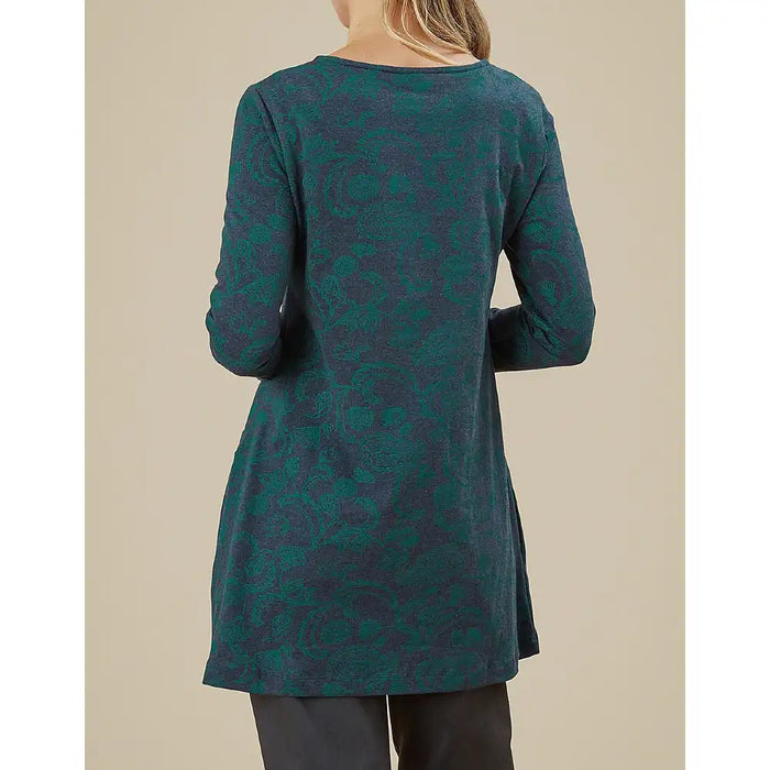 Person wearing a teal patterned long-sleeve top against a beige background