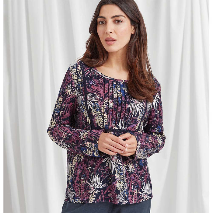 A long sleeved boat neckline top with a lace squared trim encompassing the bust with ruching detailing. Black based fabric featuring a forest flora inspired print in a mixture of purples, navy and white. 