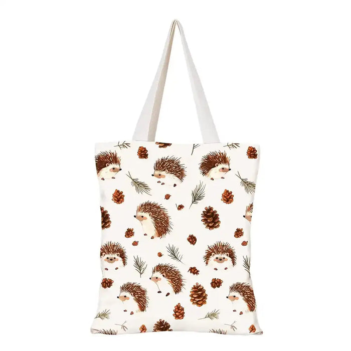 An off-white canvas tote bag with a repeating pattern of brown hedgehogs, pine cones, and evergreen branches, featuring two white shoulder straps.