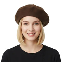 A smiling blonde woman wearing a dark brown wool beret and a black top, photographed against a clean white studio background.