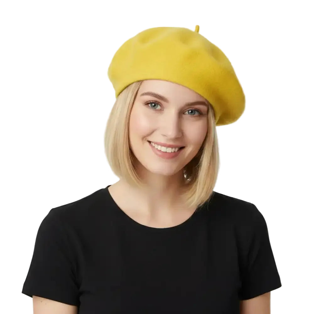 A smiling blonde woman wearing a bright yellow wool beret and a black short-sleeve top, photographed against a clean white studio background.