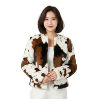 Woman with mid length bobbed hair wearing a faux fur animal design zipped jacket. She is wearing it over a white vest and white trousers. She is in a white studio environment.